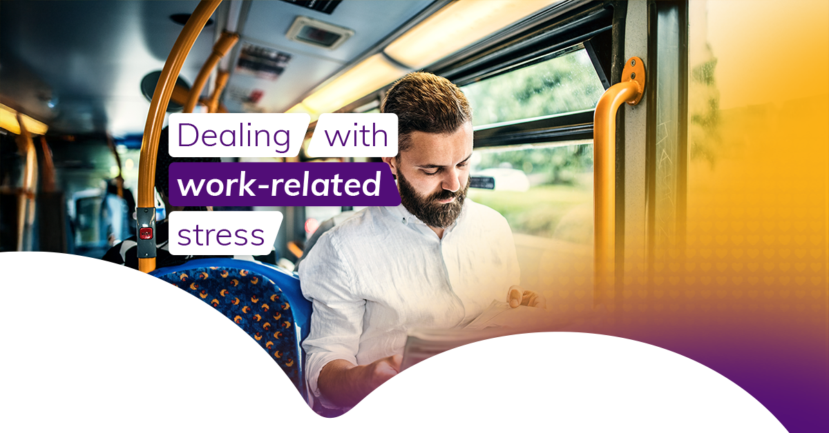 A dark-haired man sits at a window seat on a bus as he commutes to work. He reads a newspaper and wears a white shirt. The bus seats are blue and the safety poles are yellow. 